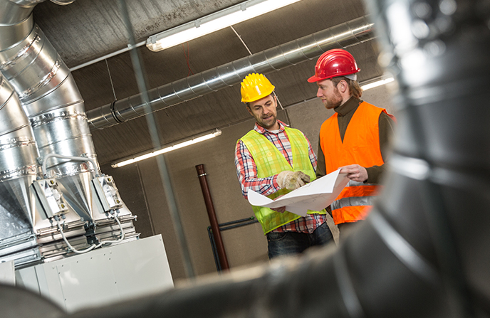 Two workers study a large-scale ducting system